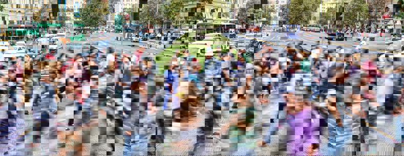 A crowd crossing a street in a busy city. The photo has been taken in slow-exposure to give an impression of movement.