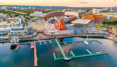 Aerial view of Cardiff Bay showing the waterfront, a Ferris wheel, the red-brick Pierhead Building, and boats moored in the marina