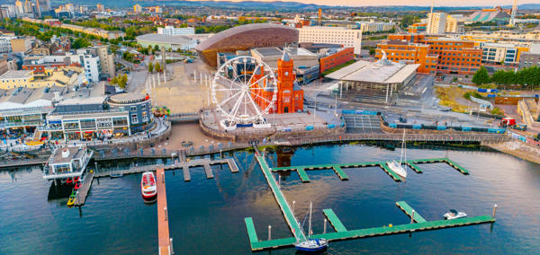 Aerial view of Cardiff Bay showing the waterfront, a Ferris wheel, the red-brick Pierhead Building, and boats moored in the marina