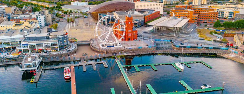 Aerial view of Cardiff Bay showing the waterfront, a Ferris wheel, the red-brick Pierhead Building, and boats moored in the marina
