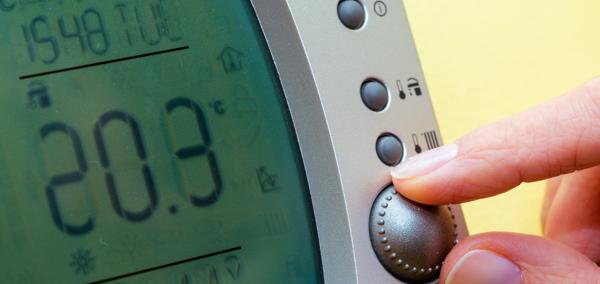 This is a close up image of fingers adjusting a domestic thermostat to a high temperature.