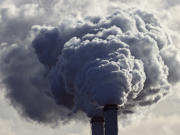 Landscape photograph of industrial chimneys emitting grey smoke. 