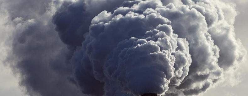 Landscape photograph of industrial chimneys emitting grey smoke. 