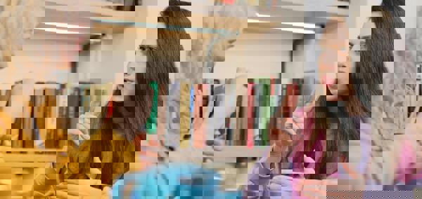 Two women sit at a table with a pot of tea, having a conversation in sign language.