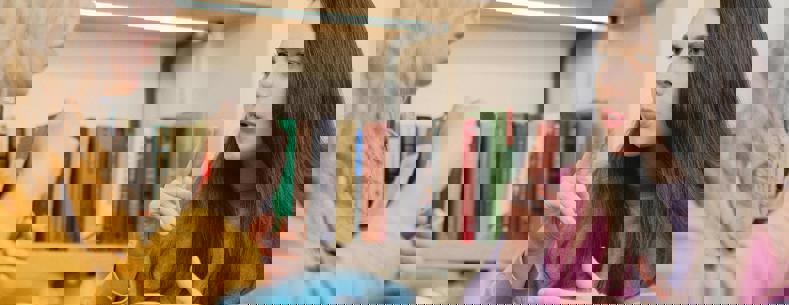 Two women sit at a table with a pot of tea, having a conversation in sign language.