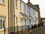 Row of newly built terraced houses with cream and blue walls, small porches, and black railings along the front