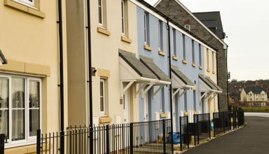 Row of newly built terraced houses with cream and blue walls, small porches, and black railings along the front
