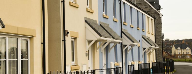 Row of newly built terraced houses with cream and blue walls, small porches, and black railings along the front