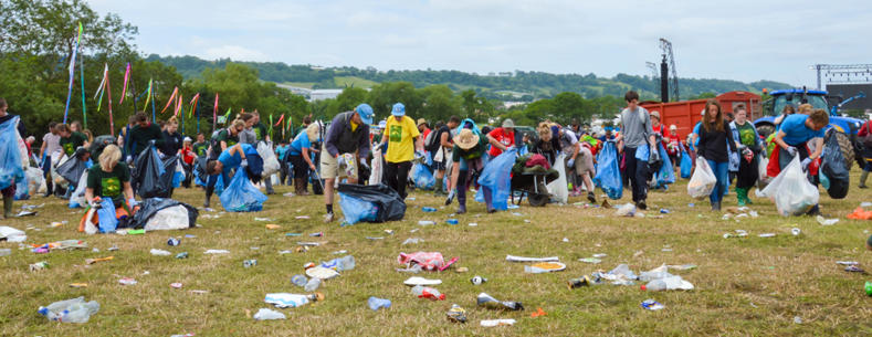 The aftermath of Glastonbury Festival: the image shows a team of litter-pickers at the campsite. The image shows empty bottles, cans, and abandoned tents strewn across the grass.