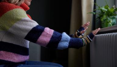 Picture of a woman putting her hands on a radiator for warmth.