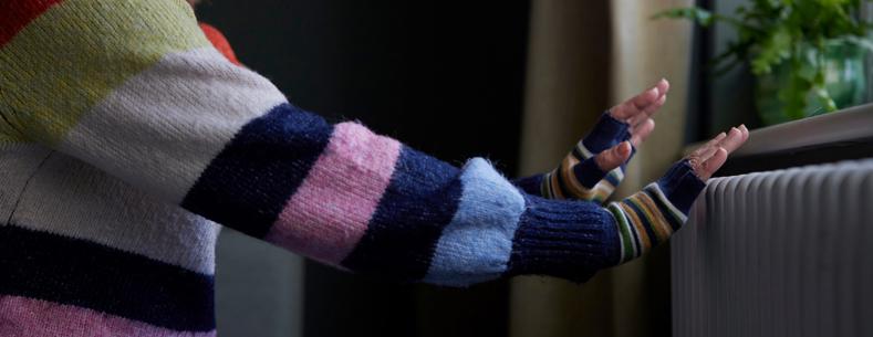 Picture of a woman putting her hands on a radiator for warmth.