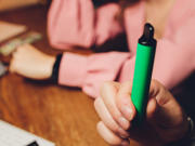 A person holding a green vape pen or e-cigarette. The focus is on the hand and the vape device 