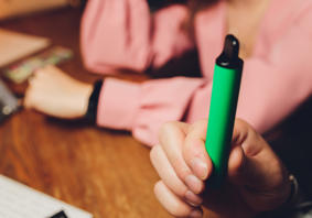 A person holding a green vape pen or e-cigarette. The focus is on the hand and the vape device 