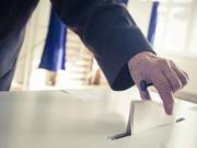 An image of a person placing a piece of paper in a ballot box.