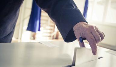 An image of a person placing a piece of paper in a ballot box.