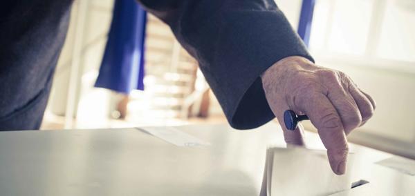 An image of a person placing a piece of paper in a ballot box.