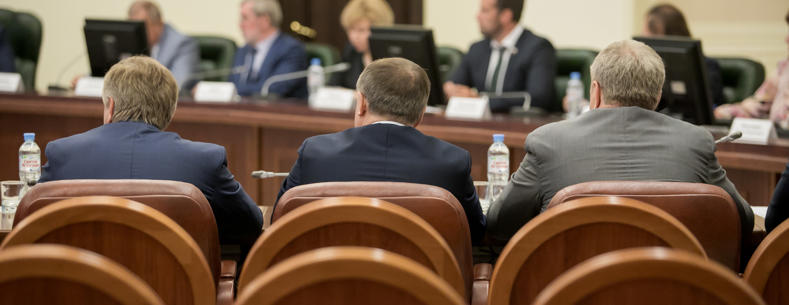 A group of smartly dressed individuals sitting in a council chamber holding a meeting