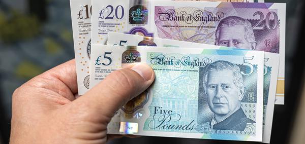 A hand holding a variety of UK bank notes, including £5, £10 and £20.