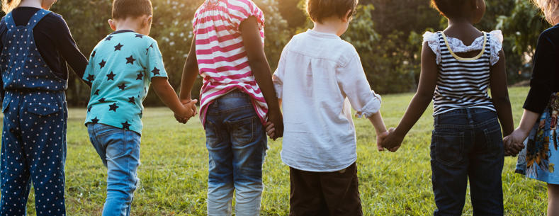 Children playing outdoors on a grassy area, with several children running and interacting in a park-like setting under natural daylight.