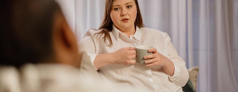 A woman holding a drink sitting opposite another person 