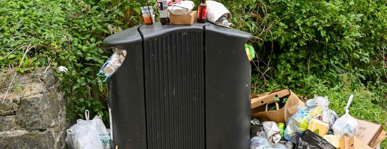 Bags, bottles and other rubbish piled up alongside a full waste bin in Newquay, Ceredigion, Wales (August 2022)