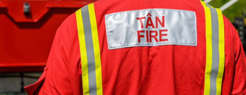 Image shows the back of a fire service employee wearing uniform with the words TÂN/FIRE 