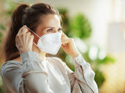 A young woman putting on a disposable face mask over her mouth and nose.