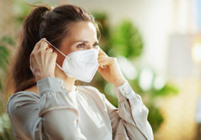 A young woman putting on a disposable face mask over her mouth and nose.