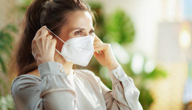 A young woman putting on a disposable face mask over her mouth and nose.