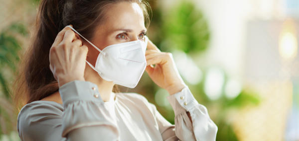A young woman putting on a disposable face mask over her mouth and nose.