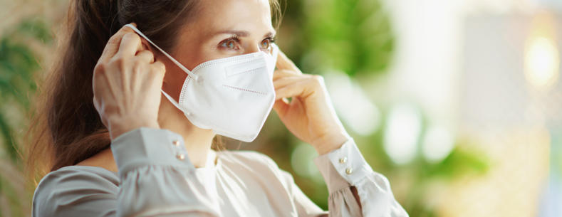 A young woman putting on a disposable face mask over her mouth and nose.