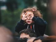 Girl sitting on an adult’s shoulders and using her hands to make binocular shape 