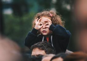 Girl sitting on an adult’s shoulders and using her hands to make binocular shape 
