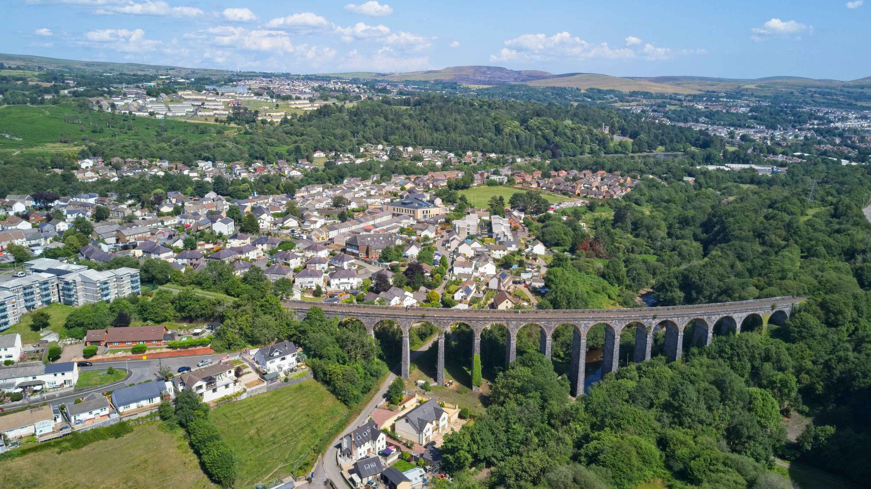 A landscape image of Merthyr Tydfil, showing houses, a bridge and other buildings as well as green space.
