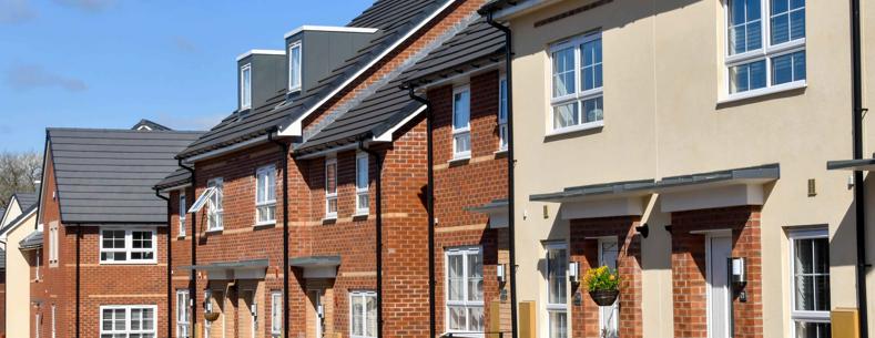 An image of a new build housing estate. The houses are predominantly terraced. The properties have some greenery and flowers outside their front doors. 