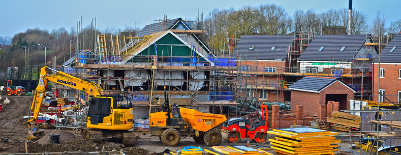 This is an image of a housing construction site with houses at various stages of construction and heavy plant machinery in the foreground.