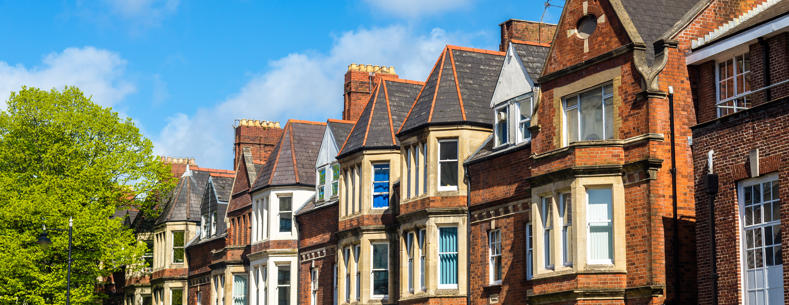 Row of traditional brick houses on a sunny day, with blue sky and a tree to the left