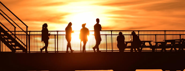 Silhouettes of people walking and sitting whilst the sun is setting over a Welsh pier.