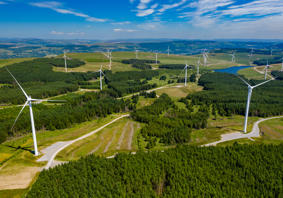 Cover image: A high angle landscape photograph of wind turbines and woodland on a hillside. 