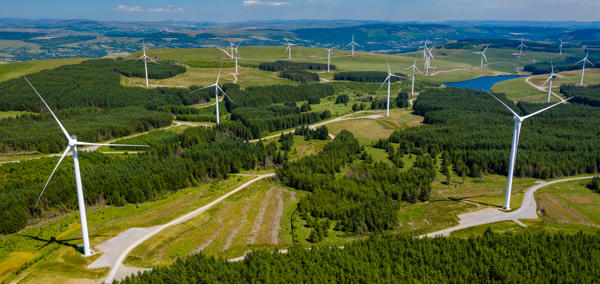 Cover image: A high angle landscape photograph of wind turbines and woodland on a hillside. 