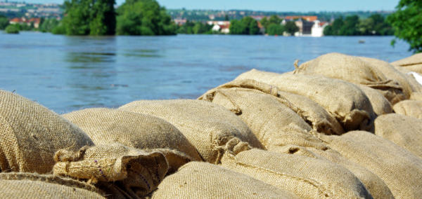 A photograph of sandbags in front of a flooded river.