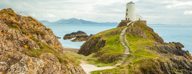 Llanddwyn Island, lighthouse, with sea and mountains in the background.