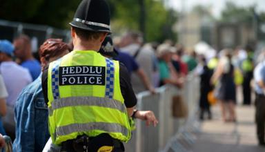 A uniformed police officer wearing a high-visibility yellow vest, standing outdoors, symbolising frontline policing and public visibility.