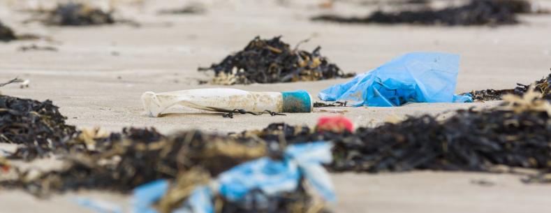 Plastic rubbish and bottle washed up on a beach and part buried in the sand an example of the many pieces of rubbish in the sea around the world