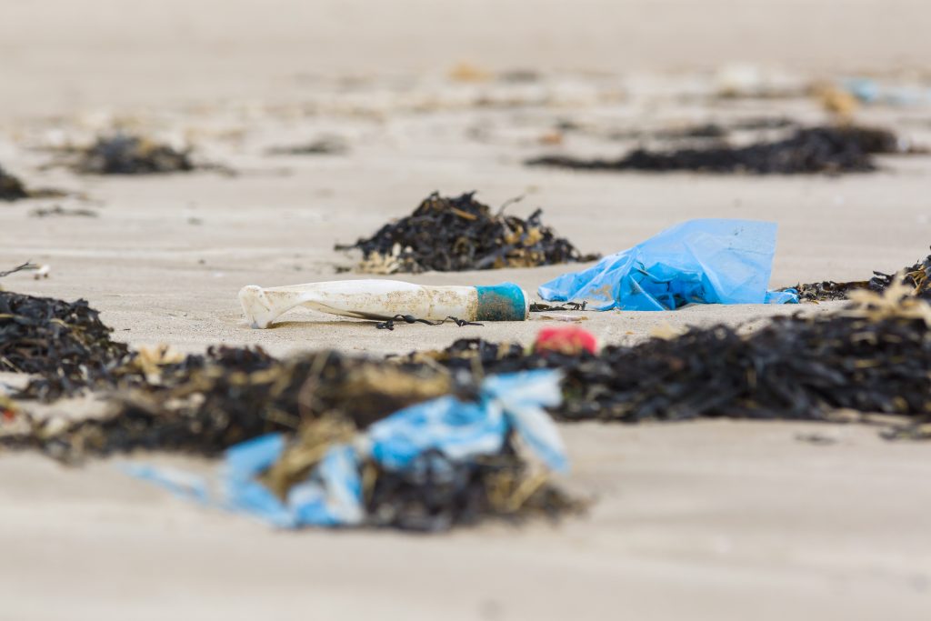 Plastic rubbish and bottle washed up on a beach and part buried in the sand an example of the many pieces of garbage in the sea around the world.